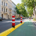 Poller LEITBOY rote und weiße Verkehrspoller auf gelber Trennvorrichtung neben grünem Fahrradweg in städtischer Straße