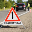 Faltsignal mit rotem Dreieck und Ausrufezeichen sowie Text POLIZEIKONTROLLE auf einer Straße mit Polizeikontrolle im Hintergrund