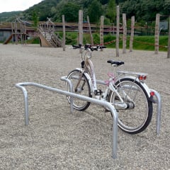 Anlehnbügelparker für Fahrräder mit einem silbernen Fahrrad auf einem Kiesplatz vor einem Spielplatz
