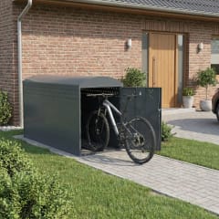 Fahrradgarage BikeBox 1 B aus Metall mit offenem Tür und Mountainbike davor, auf gepflastertem Weg vor einem Haus mit Backsteinwand