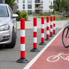 Rote und weiße Absperrpfosten FLEXPIN und FIXPIN auf Straße neben Fahrradweg und parkendem Auto