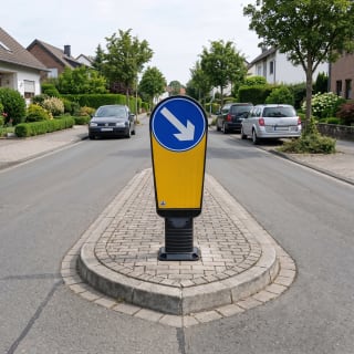 Verkehrsinselbake mit blauem Pfeilschild nach rechts auf einer Verkehrsinsel in einer Wohnstraße