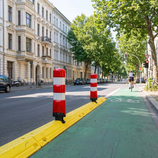 Poller LEITBOY rote und weiße Verkehrspoller auf gelber Trennvorrichtung neben grünem Fahrradweg in städtischer Straße
