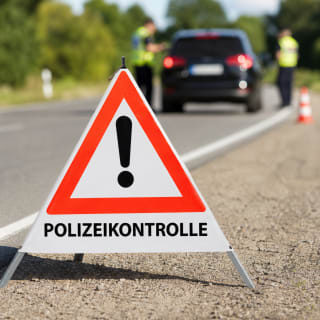 Faltsignal mit rotem Dreieck und Ausrufezeichen sowie Text POLIZEIKONTROLLE auf einer Straße mit Polizeikontrolle im Hintergrund