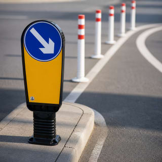 Verkehrsinselbake mit blauem Pfeil nach links unten auf gelbem Hintergrund auf einer Verkehrsinsel