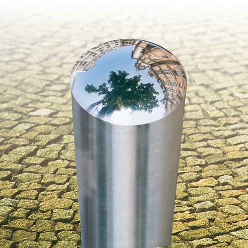 Edelstahlpoller BERLIN mit geschweißter Kappe auf gepflastertem Boden mit Spiegelung von Baum und Gebäuden