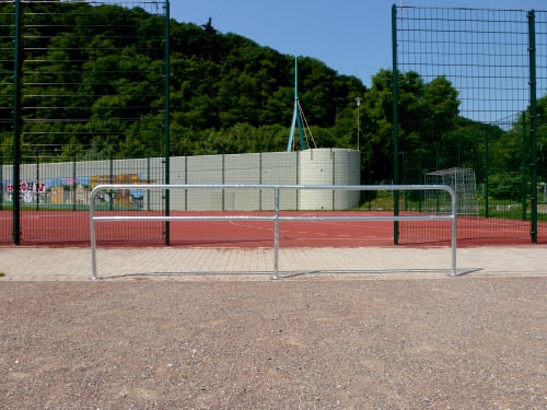 Modulares Schutzgeländer-System aus Metallrohren mit Ø 48 mm vor einem Sportplatz mit rotem Bodenbelag und grünem Zaun