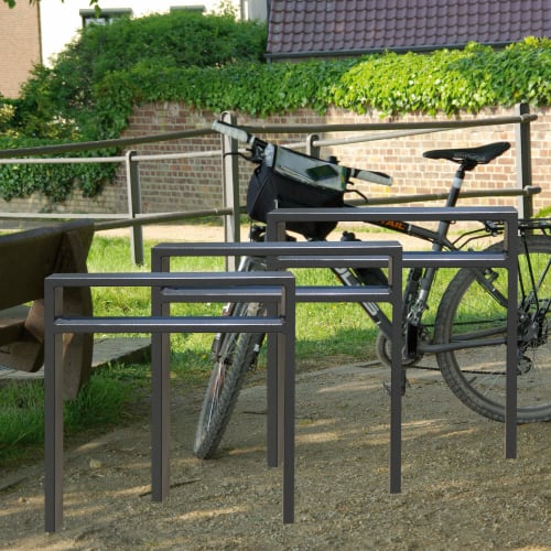 Anlehnbügel aus Stahlrohr in verschiedenen Größen vor einem Fahrrad und einer Bank im Park