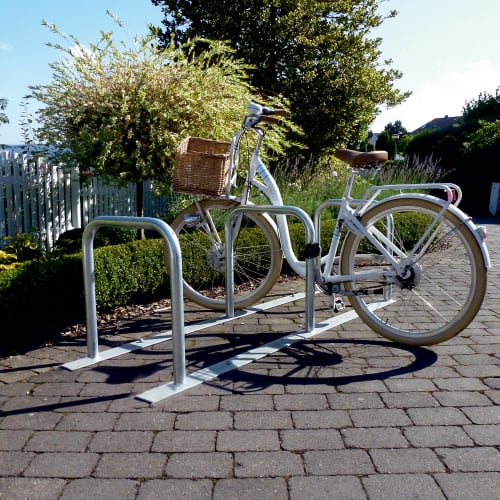 Fahrradanlehnständer-Set aus Metall mit einem weißen Fahrrad mit Korb auf gepflastertem Boden im Freien