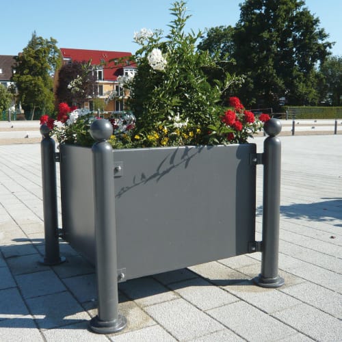 Grauer Pflanzbehälter mit Kugelkopf und bunten Blumen im Außenbereich auf gepflastertem Platz