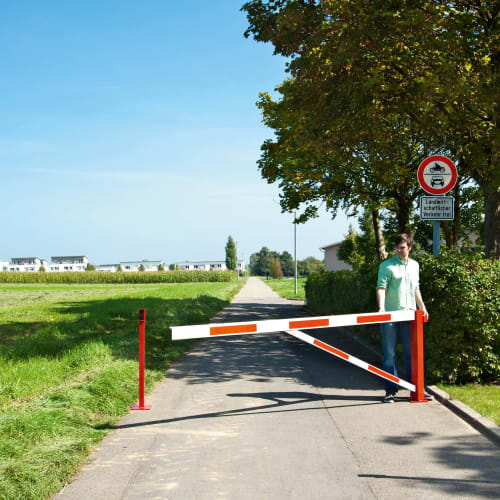 Mann öffnet rote und weiße Drehschranke COMPACT auf einem Weg mit Verkehrsschild im Hintergrund
