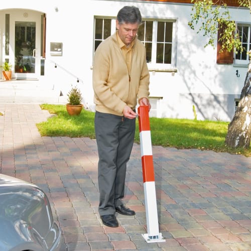 Mann sichert Einfahrt mit klappbarem Absperrpfosten SESAM in rot-weiß