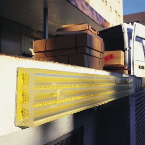 Gelber Rampenfender DAMPENING Anfahrpuffer an einer Laderampe mit Paketen im Hintergrund