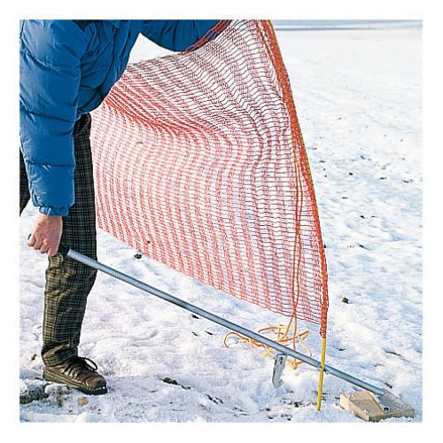 Person benutzt Erdanker-Ziehgerät zum Befestigen eines Schneefangzauns im Schnee