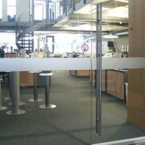 Moderne Glasdekor-Folie auf Glastür in einem Büro mit Besprechungsbereich und Spiraltreppe im Hintergrund