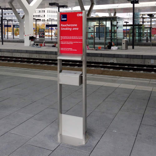 Raucherstation Columba mit 8 Liter Inhalt aus Edelstahl an einem Bahnhof mit rotem Schild Raucherzone Smoking area