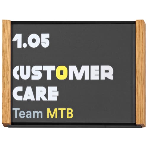 Türschild Holz LMH Studioline Edition mit der Aufschrift 1.05 CUSTOMER CARE Team MTB in weiß, gelb und grau auf schwarzem Hintergrund mit Holzrahmen