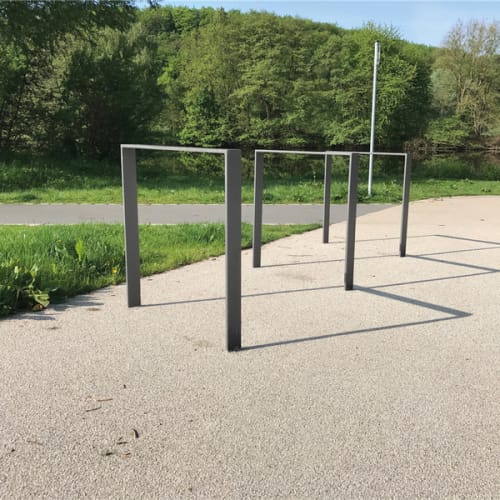 Fahrradanlehnbügel aus Flachstahl auf befestigtem Untergrund im Freien mit Grünfläche und Wald im Hintergrund