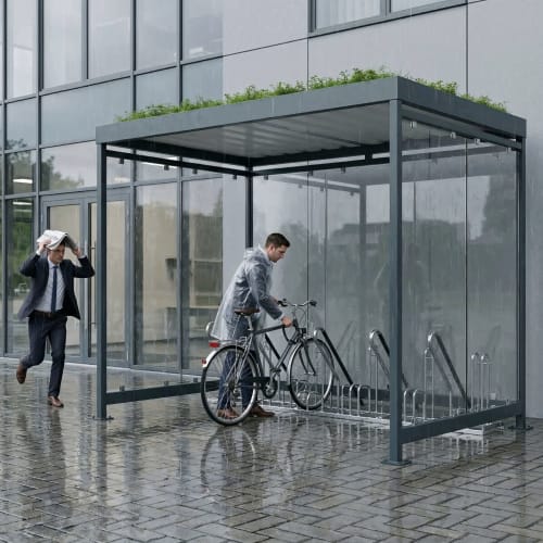 Fahrradüberdachung Köln Bike Professional Plus K3 b/b mit zwei Männern bei Regen, einer stellt Fahrrad ab, der andere hält Zeitung über Kopf