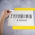 Hand hält eine transparente Bodenmarkierungstasche mit Barcode und der Nummer B-91142069 auf grauem Untergrund mit gelbem Rand