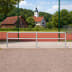 Modulares Schutzgeländer-System aus Metallrohren mit Ø 48 mm vor einem Sportplatz mit rotem Bodenbelag und grünem Zaun