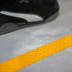 Nahaufnahme eines taktilen Bodenmarkierungsbands in Gelb auf grauem Boden mit einem schwarzen Sportschuh im Hintergrund