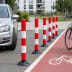 Rote und weiße Absperrpfosten FLEXPIN und FIXPIN auf Straße neben Fahrradweg und parkendem Auto