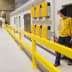 Gelbes Rammschutzgeländer XL-Line WACHTWERK X® in einer Industriehalle mit gelben Schutzkästen an der Wand und Personen im Hintergrund