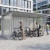 Kleine Universal-Überdachung Siegen S18 mit Fahrrädern und Personen in urbaner Umgebung, geeignet als Fahrradüberdachung oder Mülltonnenüberdachung