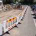 weißes Absperrgitter aus Kunststoff mit drehbaren Füßen auf einer Baustelle neben geparkten Autos