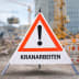 Faltsignal Warnschild mit rotem Dreieck und Ausrufezeichen, Text KRANARBEITEN, Baustelle im Hintergrund