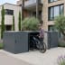 Fahrradgarage BikeBox 1 G XL aus Metall mit geöffnetem Fach, in dem ein Mann mit Fahrradhelm ein E-Bike abstellt, moderne Wohnhausfassade im Hintergrund
