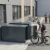 Fahrradgarage BikeBox 1 G mit Münzpfandschloss aus Metall, geöffnete Tür, Mann mit Fahrrad und Helm neben der Garage