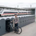 Mann mit Fahrradhelm stellt Fahrrad in Fahrradgarage BikeBox 1 B mit Münzpfandschloss an Bahnhof ab