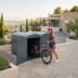 Frau stellt pinkfarbenes Mountainbike in Fahrradgarage BikeBox 1 B als Komplett-Set aus Metall vor modernem Haus ab