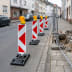 TL Leitbake FUTURE Typ S Absperrung mit roten und weißen diagonalen Streifen und gelben Warnleuchten auf einer Straße neben einer Baustelle