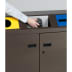 Wertstoff-Sammelstation WS 97 mit drei Fächern in braun, gelb und blau, Hand wirft schwarzen Müllbeutel ein