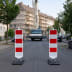 Sperrbake Typ D geblockt mit roten und weißen Streifen auf einer Straße vor einem Kran und Baustelle