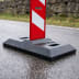 Schwarze Fußplatte aus Kunststoff mit roter und weißer Flachbake auf nassem Asphalt