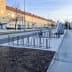 Fahrradständer Epsilon® Plus aus Metall auf einem Bürgersteig mit mehreren Fahrrädern, städtische Umgebung mit gelben Wohngebäuden im Hintergrund