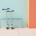 Zwei silberne Roller in einem Rollerständer Scooter-Parker Rulo vor einer türkisfarbenen und orangefarbenen Wand