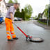 Mann hebt Kanaldeckel mit NESTLE Kanaldeckelheber auf einer Straße in Wohngegend