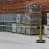 Gurtabsperrpfosten Beltrac Storetrac Double mit drehbarer Gurtkassette und gelbem Absperrband vor Lager mit Metallcontainern