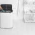 Weißer Soft-Touch Mülleimer Bo Touch Bin von Brabantia mit 2x 30 Liter Inhalt, geöffnet und mit einer Hand, die eine Flasche hineinwirft