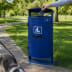 Blauer Stand-Abfallbehälter mit integriertem Beutelspender und Ascher, 70 Liter Fassungsvermögen, im Park mit Hand, die Hundekotbeutel entsorgt